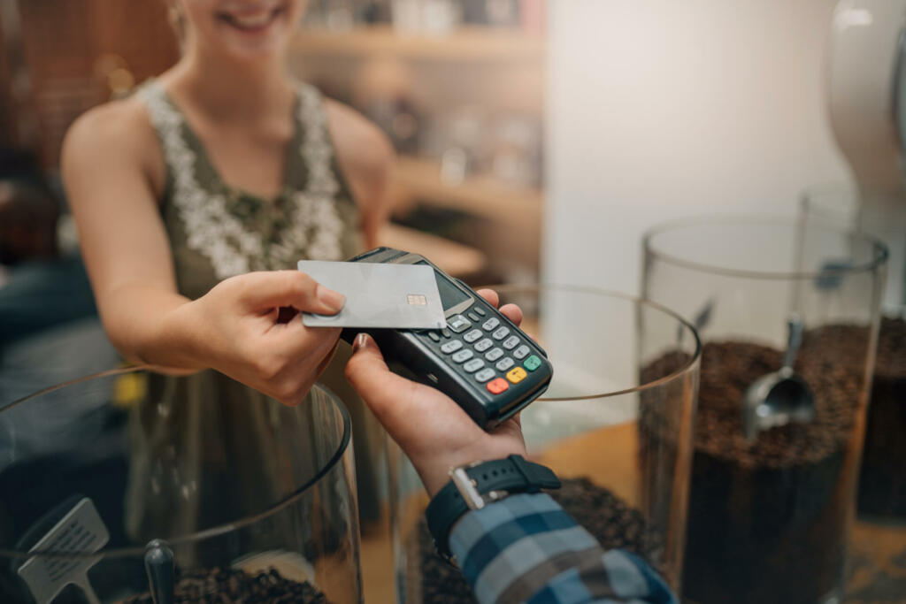 Hand of customer paying with contactless credit card with NFC technology. Waiter with a credit card reader machine and with female smiling holding credit card. Focus on hands