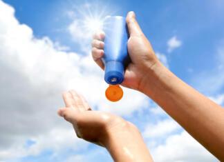 Bodi kreativen in nosi kremo za sončenje! Hand of female holding sunscreen. Very sun light Sky background.Health concepts and skin care