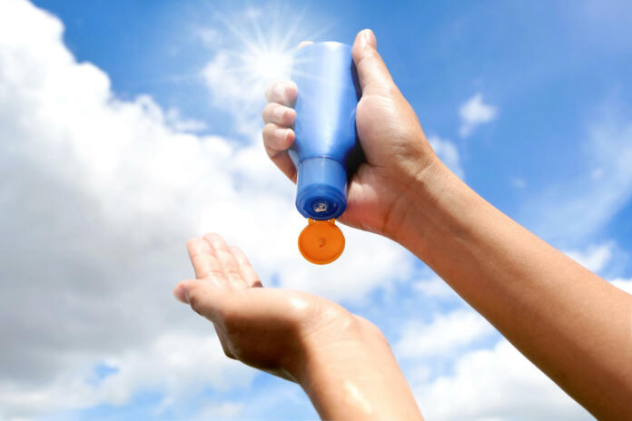 Hand of female holding sunscreen. Very sun light Sky background.Health concepts and skin care