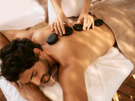 Handsome man at spa resort receives hot stone massage. Hot stone massage therapy using smooth, flat, heated stones