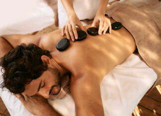 Masaža Handsome man at spa resort receives hot stone massage. Hot stone massage therapy using smooth, flat, heated stones