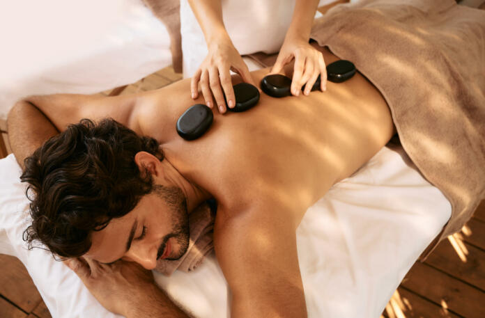 Handsome man at spa resort receives hot stone massage. Hot stone massage therapy using smooth, flat, heated stones