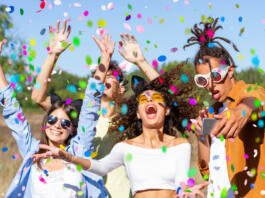 Happy excited friends having fun outdoor celebrating with confetti - Young millenial people enjoying summertime together at garden party - Cheerful friendship concept. Party - festival concept.