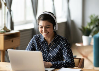 Nina Pušlar: POVEŽITE ŠTUDIJ S SVOJIMI INTERESI Happy indian young girl student wear headphone watch webinar listen online course communicate by conference video call e learn language in app laugh study with teacher lesson look at laptop at home