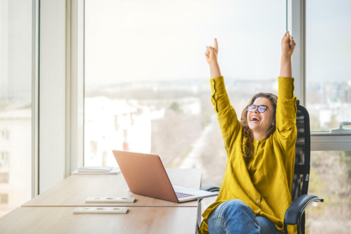 Happy successful businesswoman in yellow shirt raising fists with ambition. Woman going up career ladder. Business achievement and promotion concept