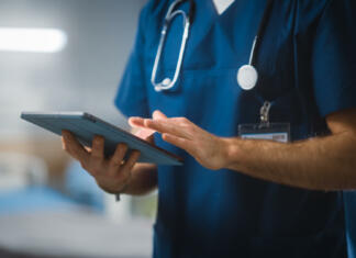 Zdravje študentov Hospital Ward: Unrecognizable Head Nurse, Doctor, Surgeon Uses Digital Tablet Computer Health Care Vitals Monitoring Computer Machine. Modern Clinic with Advanced Equipment and Professional Working