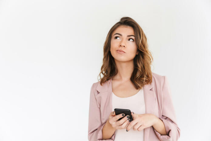 Image of young cute beautiful lady standing isolated over white wall background looking aside using mobile phone.