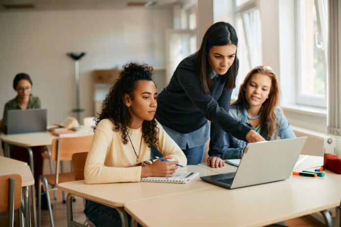 IT teacher and her students using laptop during computer class in high school.