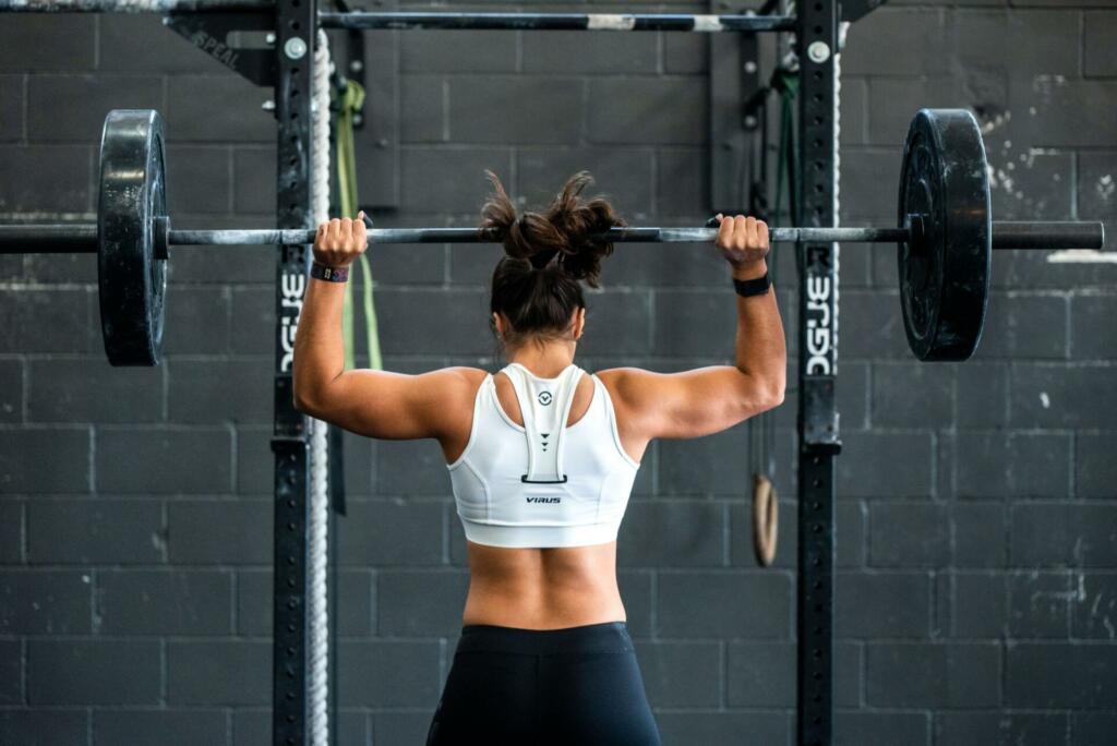 ženska drži palico z utežmi v fitnesu