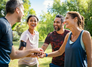 ŠOU šport = študentski šport = zdrava zabava Laughing mature and multiethnic sports people putting hands together at park. Happy group of men and beautiful women smiling and stacking hands outdoor after fitness training. Multiethnic sweaty team cheering after intense training.