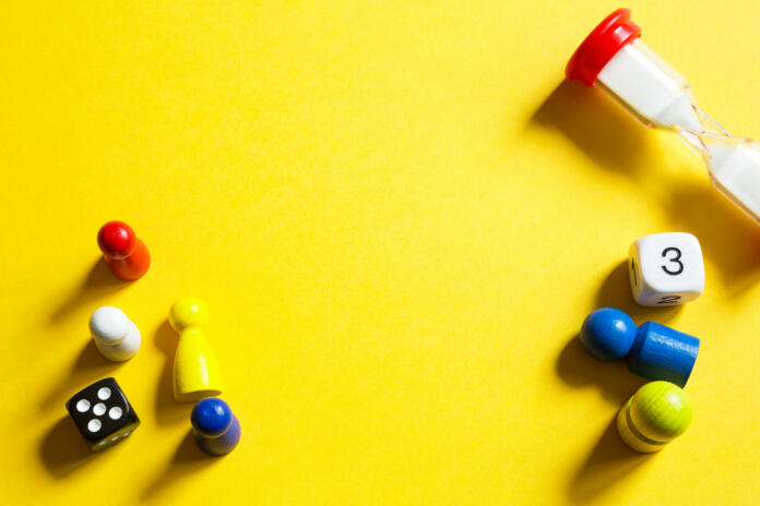 Layout of board games on a yellow background: dice, chips, hourglass timer. Entertainment at home for children and adults. Copy space