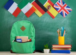 Študentom gre najbolje v Nemčiji Learning languages concept - green backpack, flags of Spain, France, Great Britain and other countries, books and school supplies on the background of the blackboard