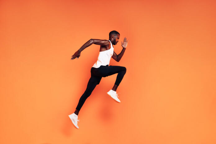 Male runner doing fitness workout. Athlete exercising over an orange background.