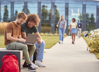 Število študentov v Sloveniji padlo pod 80.000 Male University Or College Students Sitting Outdoors On Campus Talking And Working On Laptop