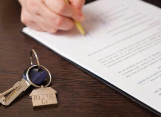 Avtorska pogodba in davek Man client signs new apartment purchase contract with pen near keys with house shaped breloque put on table extreme close view