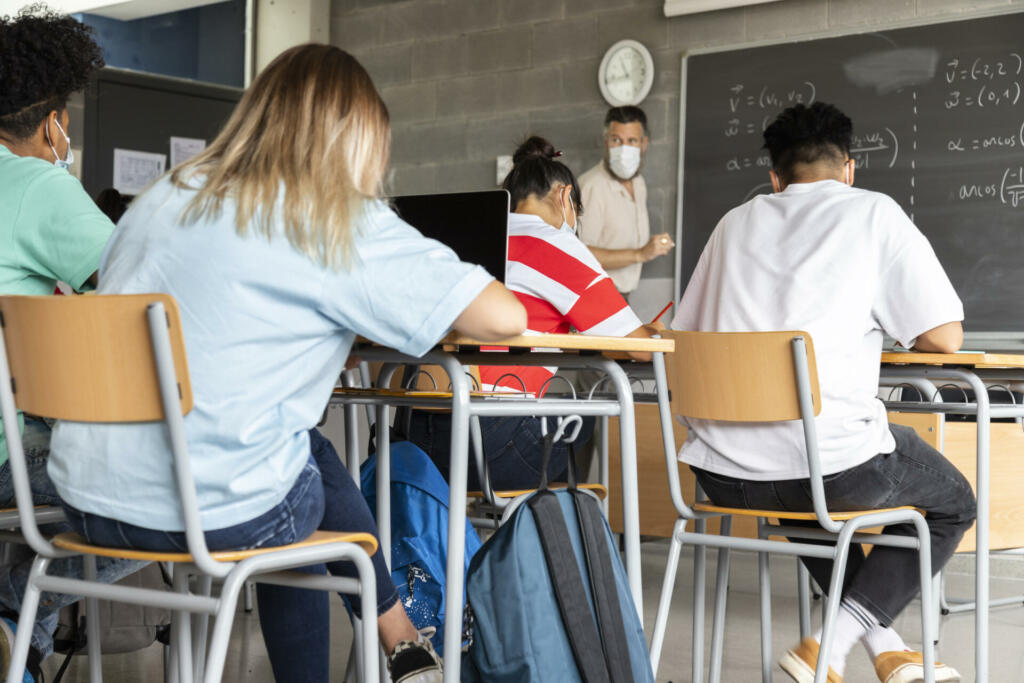 Mathematics class. Mature white male teacher wearing face mask in classroom with group of multiracial teen high school students. Education concept. Healthcare concept.