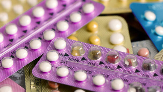 Oral contraceptive pill on pharmacy counter with colorful pills strips background.