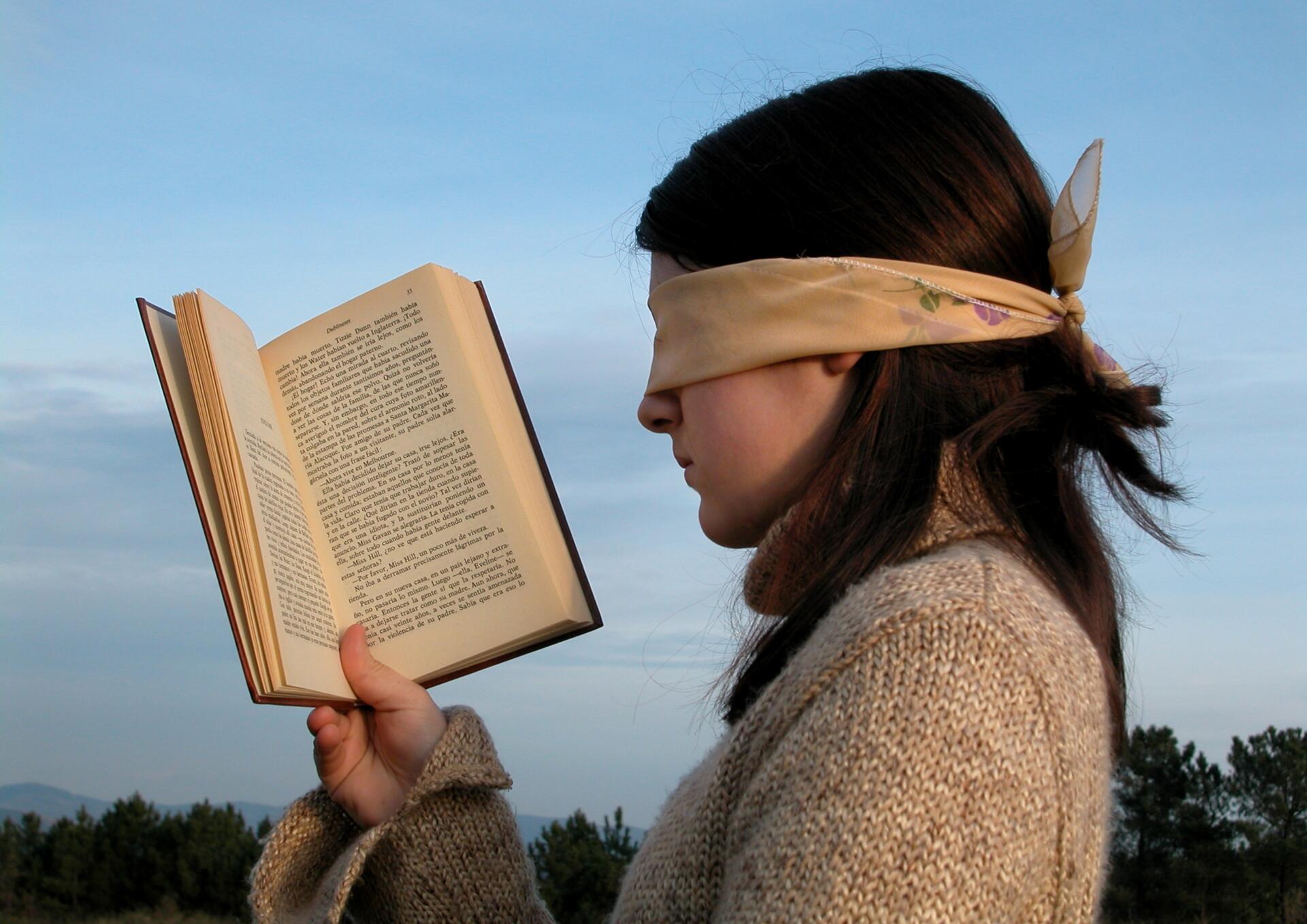 Ženska s prevezo čez očmi v rokah drži knjigo