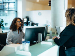 Receptionist assisting a woman standing at front desk. Woman standing at the reception talking with a friendly receptionist behind the desk of municipality office.