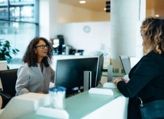Vračanje socialne pomoči Receptionist assisting a woman standing at front desk. Woman standing at the reception talking with a friendly receptionist behind the desk of municipality office.
