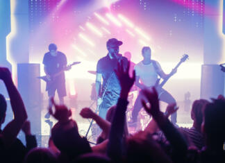 Ne bi bil rad profesor s tišino Rock Band with Guitarists and Drummer Performing at a Concert in a Night Club. Front Row Crowd is Partying. Silhouettes of Fans Raise Hands in Front of Bright Colorful Strobing Lights on Stage.