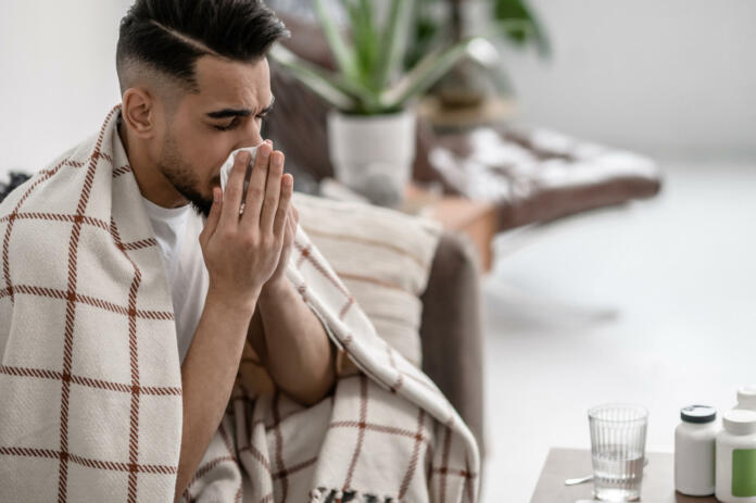 Running nose. A dark-haired man having a flue and cleaning his nose