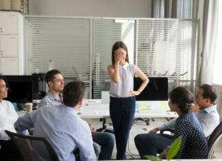 5 nasvetov za samozavestnejši javni nastop Shy nervous bashful female employee feels embarrassed blushing afraid of public speaking at corporate group team meeting, timid stressed woman hiding face during awkward moment reporting in office