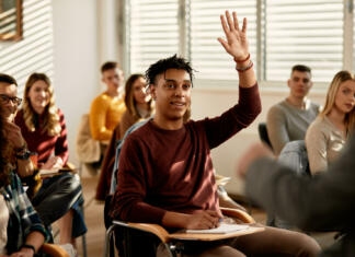 Izredni srednješolski programi izobraževanja Smiling African American student raising his hand to ask a questing during a class at lecture hall.