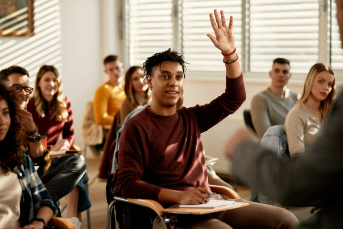 Smiling African American student raising his hand to ask a questing during a class at lecture hall.