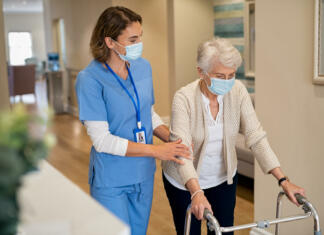 SOCIALNO PODJETNIŠTVO: PRILOŽNOST ZA REŠEVANJE BREZPOSELNOSTI PRI MLADIH Smiling nurse with face mask helping senior woman to walk around the nursing home with walker. Young lovely nurse helping old woman with surgical mask for safety against covid-19 using a walking frame in hospital corridor. Friendly caregiver and elderly patient walking in hallway wearing protective face mask during covid pandemic.
