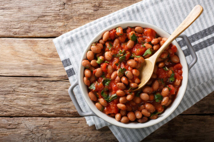 Stewed cranberry beans or borlotti in tomato sauce with herbs close-up in a bowl on the table. horizontal top view from above