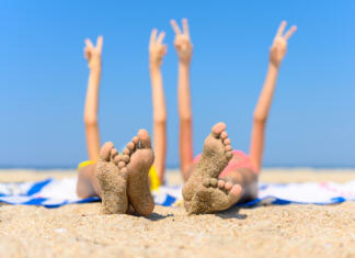 SONČENJE The concept of a wonderful seaside holiday. Children's feet with adhered sand against the background of the sea and raised hands. Selective focus and shallow depth of field.