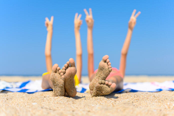 The concept of a wonderful seaside holiday. Children's feet with adhered sand against the background of the sea and raised hands. Selective focus and shallow depth of field.