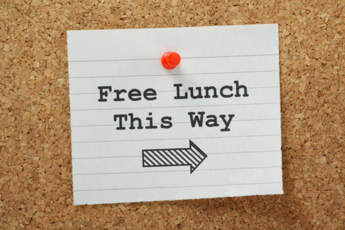 The phrase Free Lunch This Way typed on a piece of lined paper and pinned to a cork notice board