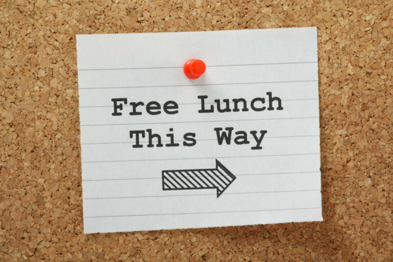 The phrase Free Lunch This Way typed on a piece of lined paper and pinned to a cork notice board
