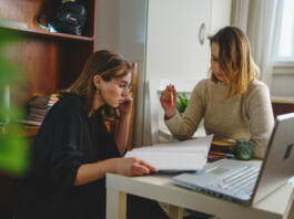 two women young caucasian female student sitting at home with her mentor teacher looking to the notebook explaining lesson study preparing for exam learning education concept real people copy space