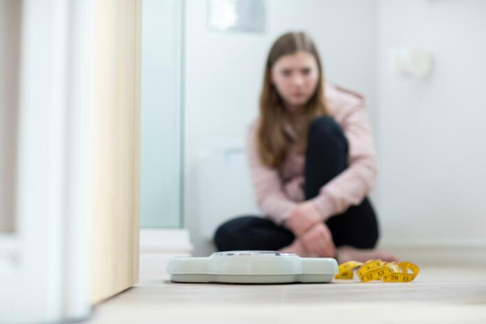 Unhappy Teenage Girl Sitting In Bathroom Looking At Scales And Tape Measure