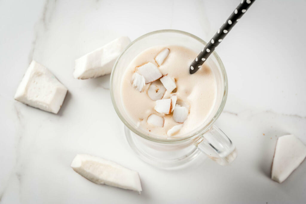 Vegan food. Refreshing summer cocktails. beverages. Coconut latte smoothie - with coffee, coconut cream (milk), pieces of coconut. On a white marble kitchen table. Copy space