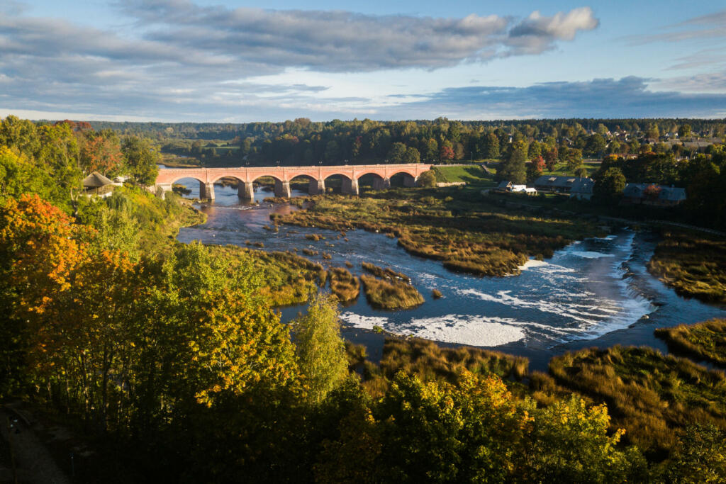 Venta Rapid waterfall, the widest waterfall in Europe and long red brick bridge in sunny autumn morning, Kuldiga, Latvia. Captured from above.