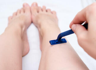 Odstranite nehvaležne dlačice Woman shaving legs with a blue disposable plastic razor close up, unwanted hair removing.