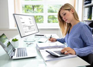 Razkorak med spoloma v digitalni industriji še vedno velik Young Businesswoman Calculating Bill With Computer And Laptop On Desk
