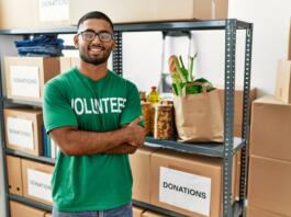 Young indian man volunteer holding donations box happy face smiling with crossed arms looking at the camera. positive person.