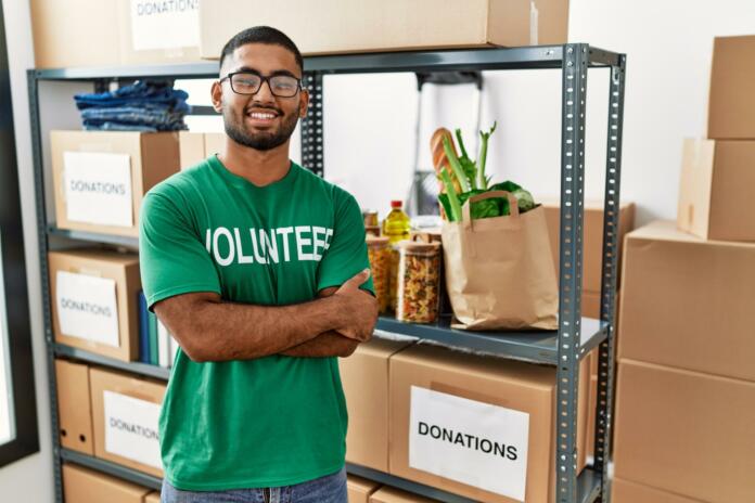 Young indian man volunteer holding donations box happy face smiling with crossed arms looking at the camera. positive person.