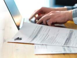 Young man writing college or university application form with laptop. Student applying to school. Scholarship document, admission paper or letter on table. Typing email. Education and communication.