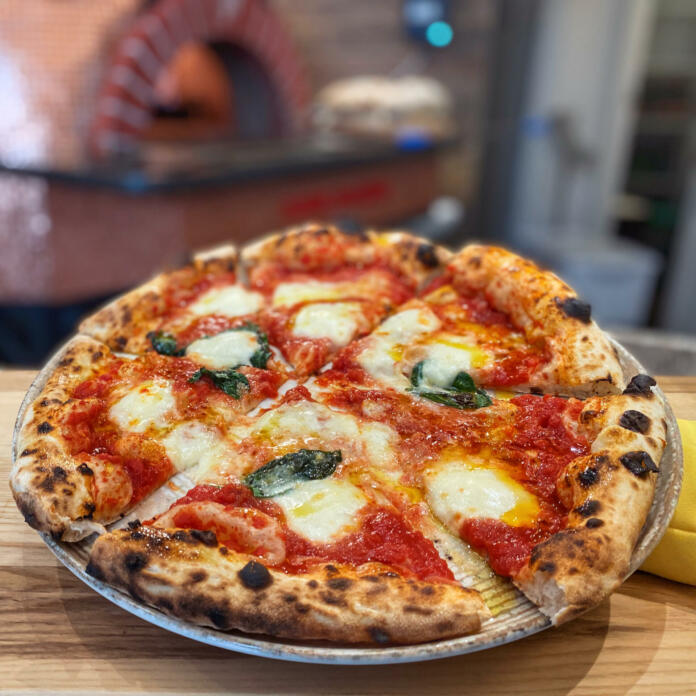 a freshly baked margherita pizza, with mozzarella, tomato and basil. The wood-burning oven in the Neapolitan pizzeria is spectacular