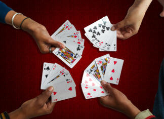 Zabavne igre s kartami A high angle view of the four hand-held playing cards on a maroon background