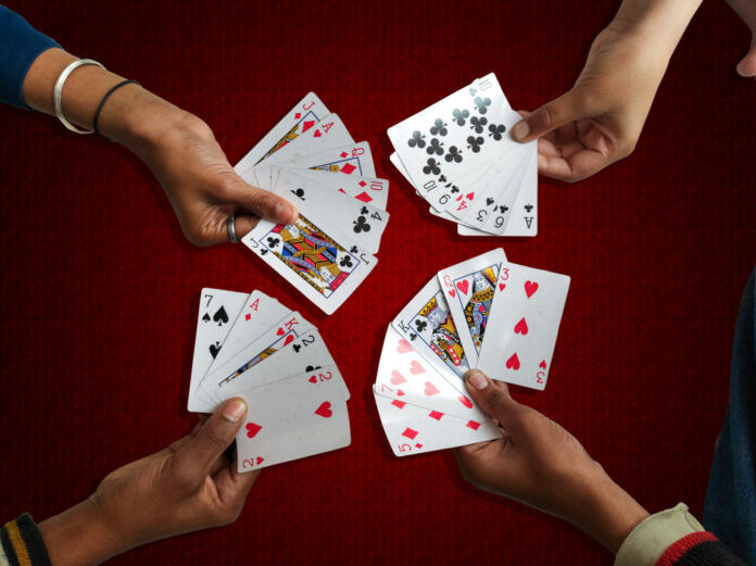 A high angle view of the four hand-held playing cards on a maroon background