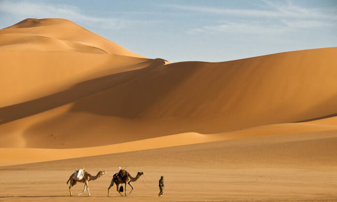 a-man-with-camels-in-the-sand-dunes-desert-of-libya-stockpack-istock a man with camels in the sand dunes desert of Libya.
