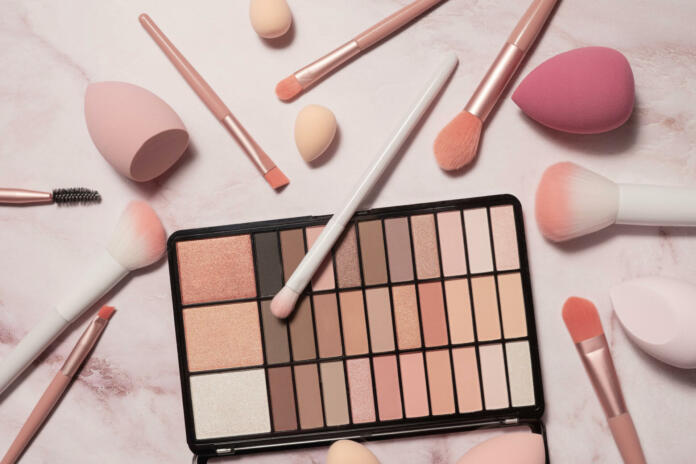 A nude eyeshadow palette and makeup artist's tools on a marble vanity. Brushes for powder, blush, eyebrows, shadows and sponges for concealer and foundation.