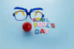 April Fools Day text and funny glasses on blue background.